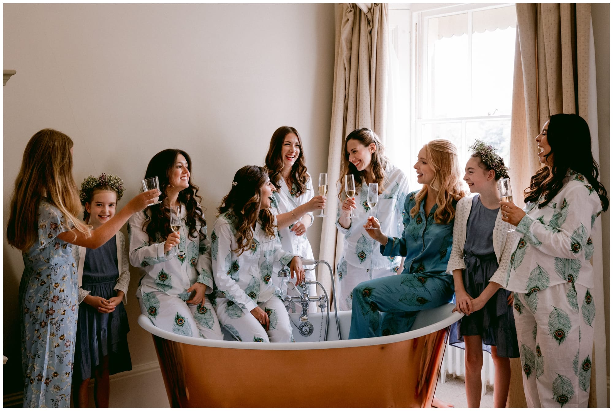 Bridesmaids sitting and laughing on the edge of a copper bathtub Sibton Park Wedding Photography